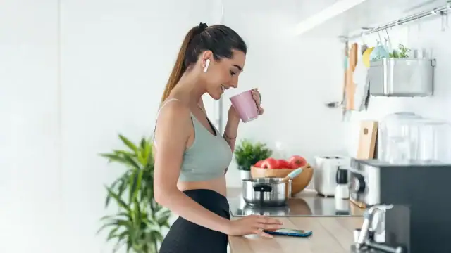 Woman in a sports bra and earphones enjoys a cup of coffee, showcasing a blend of fitness and relaxation.