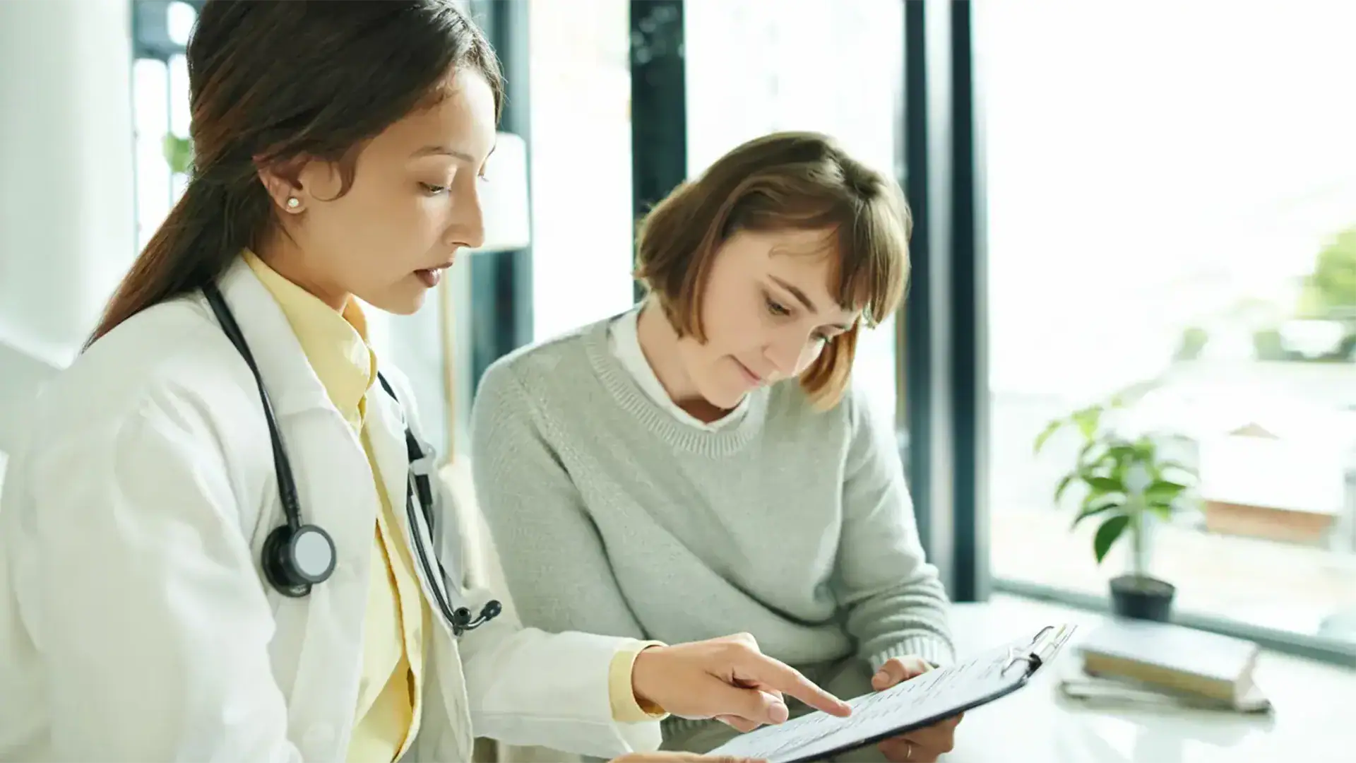 A woman and a doctor are seated at a table, engaged in a discussion about health-related topics.