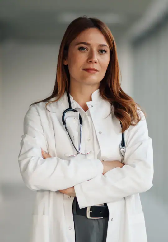 A female healthcare professional wearing a white lab coat and stethoscope stands with her arms crossed.