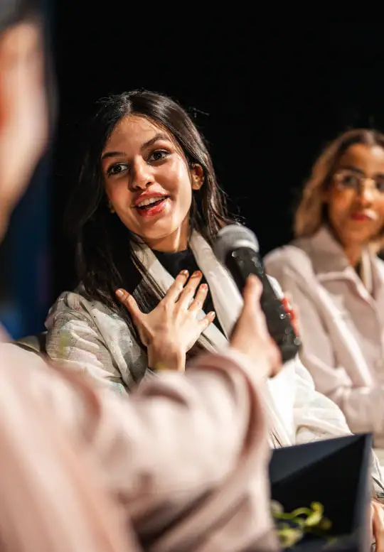 A woman speaks during a panel discussion while responding to a microphone.