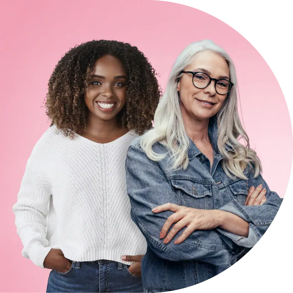 Two women of different generations stand together smiling against a pink background, representing confidence, connection, and women's wellness across life stages.