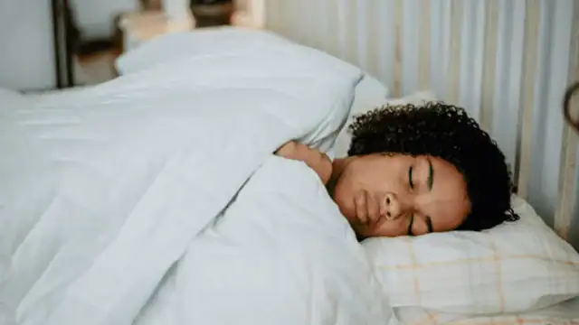 Woman peacefully sleeping in bed, covered by a soft white blanket.