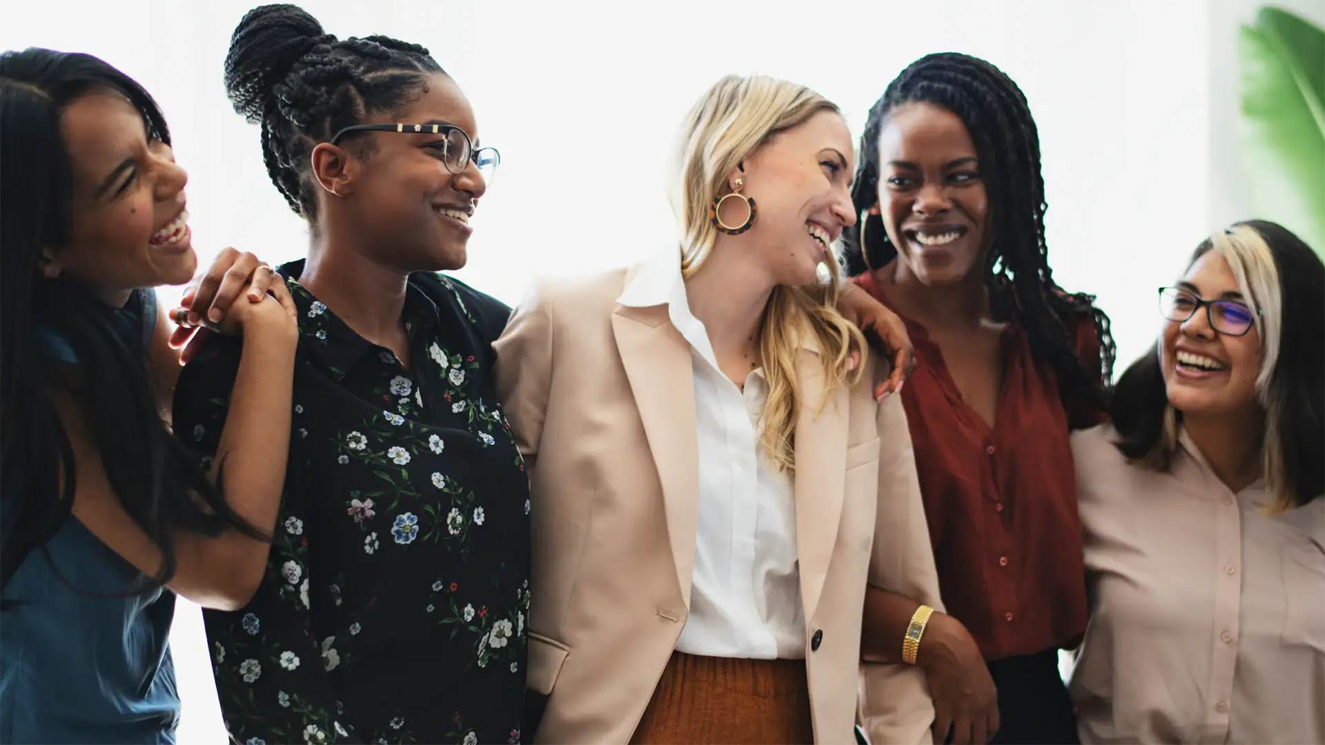 Diverse group of five women smiling and laughing together, representing community, connection, and support.